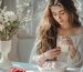 a young woman is opening a new perfume box sitting at the table with plates of sweets and berries on it