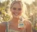 A gorgeous woman in the middle of a garden smiling and holding a glass perfume bottle with a Vanilla label