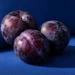 Three dark-purple plums with pale natural bloom