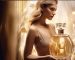 fashion magazine ad for an expensive niche perfume featuring a blonde woman in an elegant gold dress standing next to the iconic glass bottle