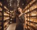 A woman in an elegant dress is surrounded by shelves of luxury perfume bottles