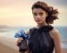 model is holding an elegant blue bottle and bow on it posing in front of a beach backdrop