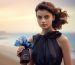 model is holding an elegant blue bottle and bow on it posing in front of a beach backdrop