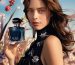 model is holding an elegant blue perfume bottle posing in front of a floral field